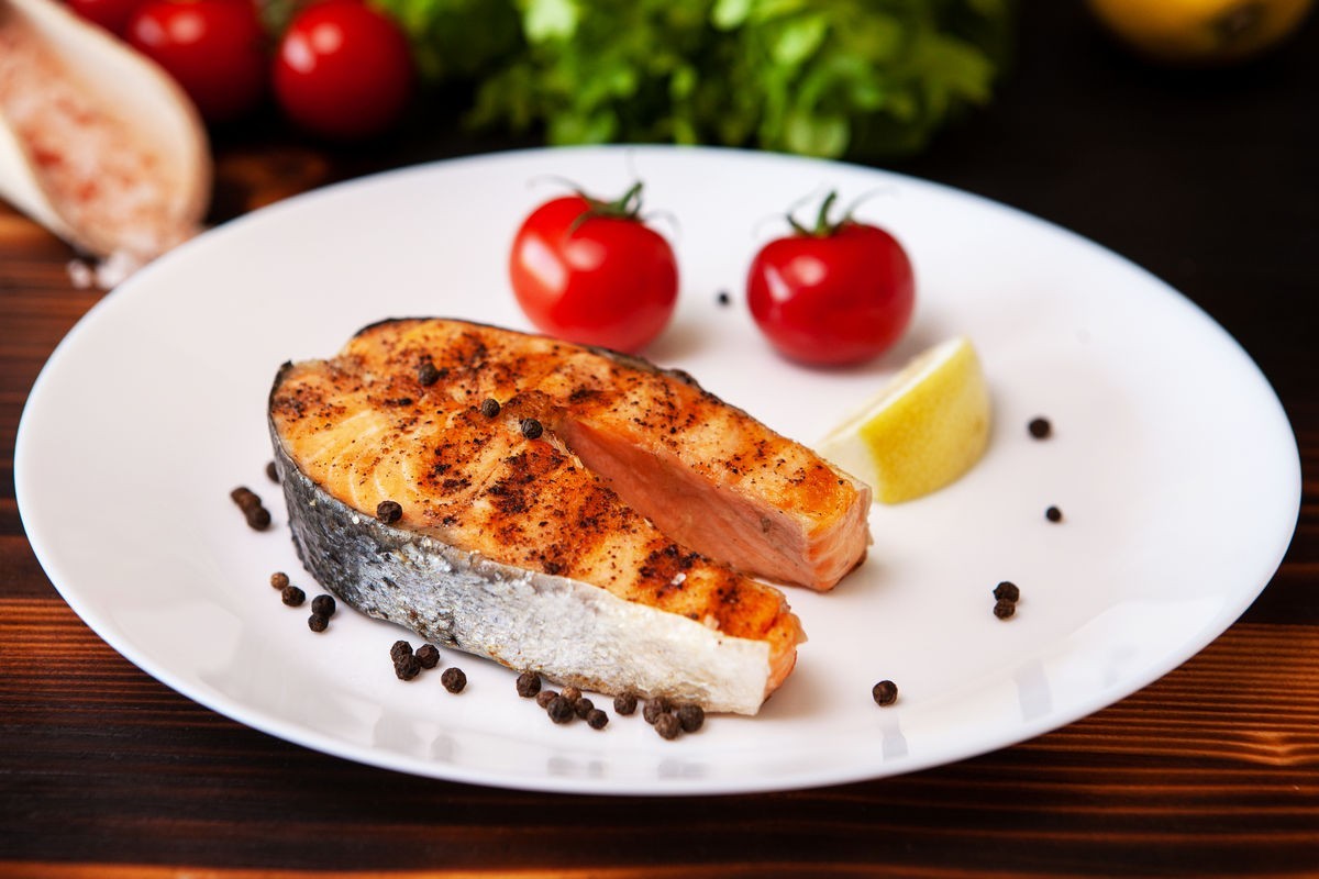 Slice of salmon on a white plate with peppercorns tomatoes and a lemon slice